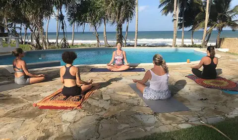 Women meditating on mats beside the pool