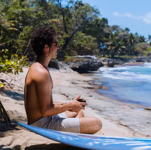 Man sitting cross legged on a surfboard on a rocky beach