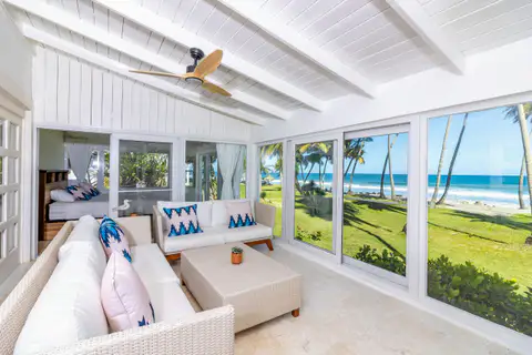 Sunroom living area with white sofas and ocean views through glass walls