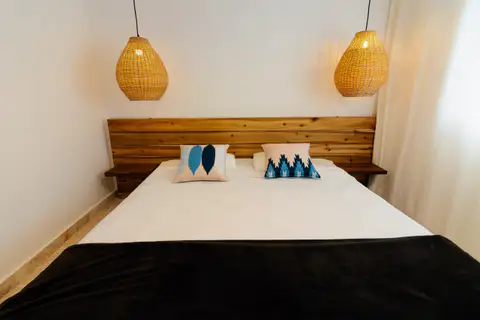 Double bed with a black blanket under two woven pendant lamps