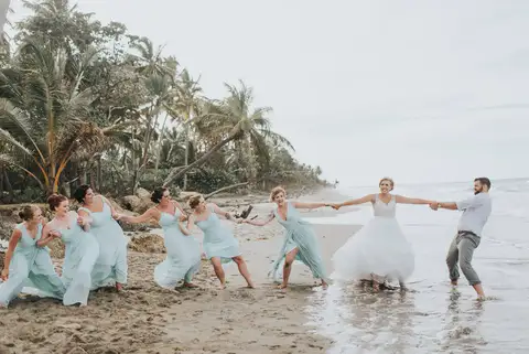 Bridal party in turquoise dresses pulling the groom through the shallows in a playful tug of war